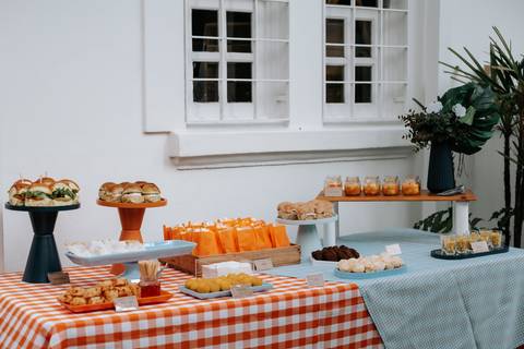 Foto de mesa de buffet com sanduíches e petiscos decorada com toalha xadrez.'