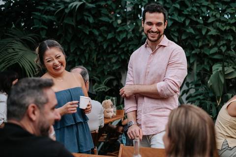 Foto dos pais sorrindo e conversando com convidados no jardim.'