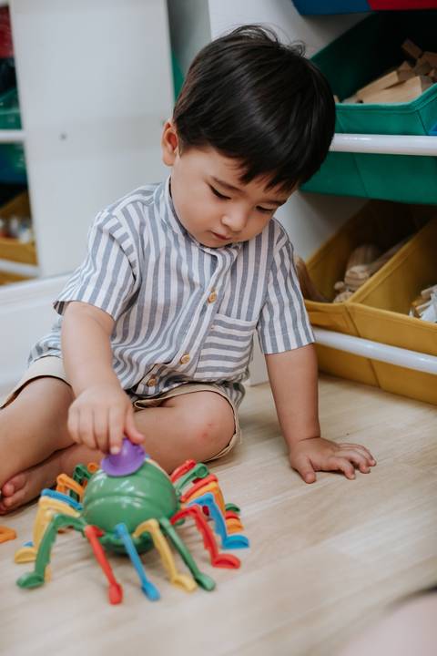 Foto do Arthur concentrado brincando com peças coloridas no chão.'