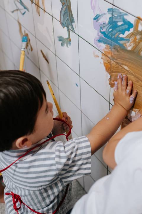 Foto em detalhe do Arthur concentrado pintando azulejos com pincel.'