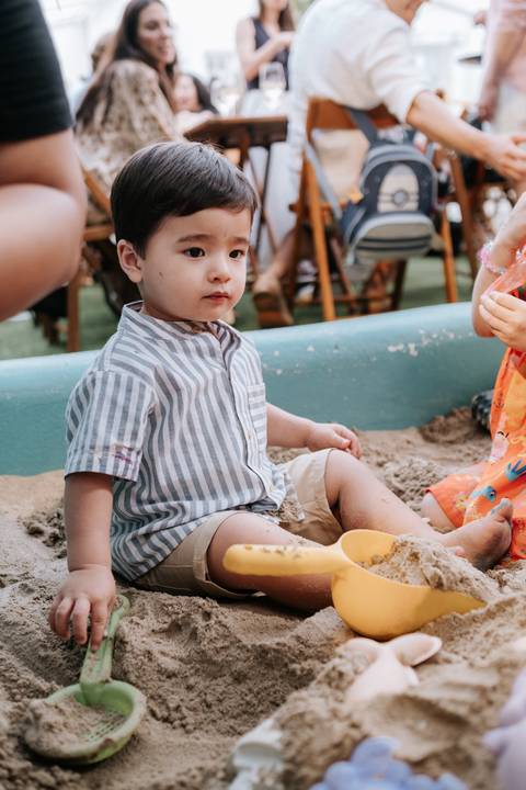 Foto do Arthur sentado na areia com seus brinquedos de praia.'