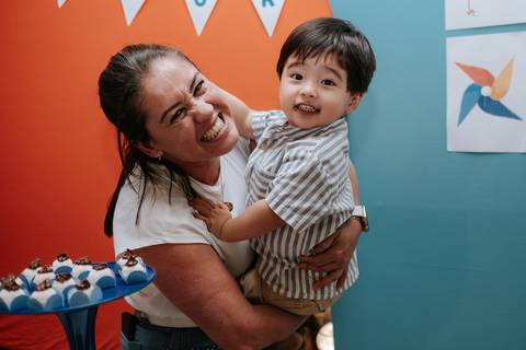Foto do aniversariante no colo de uma convidada sorridente na decoração.'