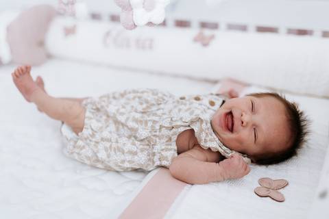 Foto da bebê Olívia espreguiçando e sorrindo enquanto descansa.'