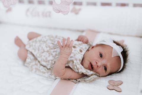oto aproximada da bebê com laço branco na cabeça olhando para a câmera.'