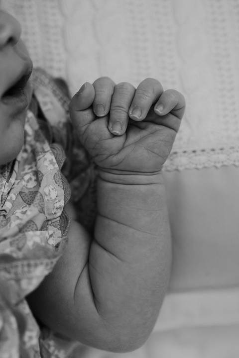 Foto em preto e branco destacando o detalhe do pulso e mão da bebê.'