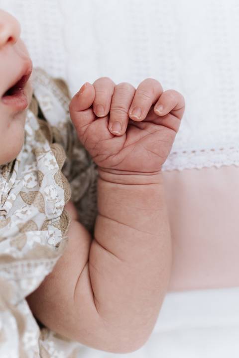 Foto em detalhe das dobrinhas e da mãozinha da recém-nascida.'
