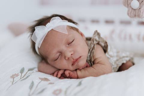 Foto da bebê dormindo profundamente com as mãos sob o rosto.'