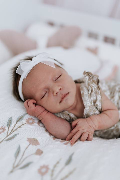 Foto aproximada da bebê em sono tranquilo sobre manta bordada.'