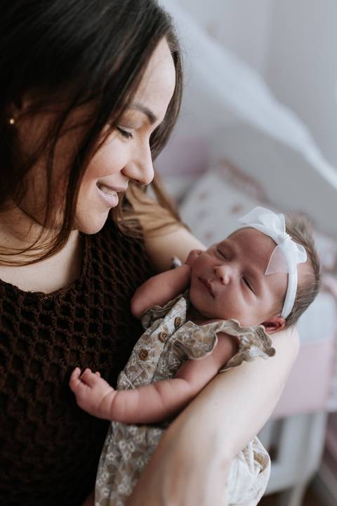 Foto da mãe sorridente com a bebê descansando em seu peito.'