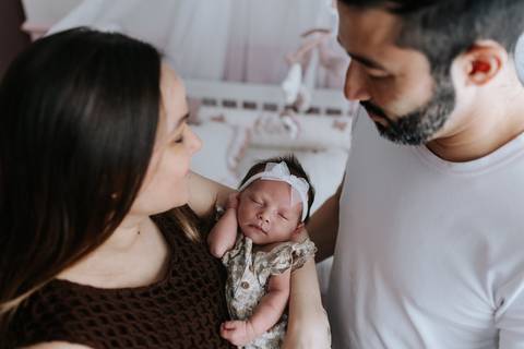Foto do casal observando a filha recém-nascida no colo da mãe.'