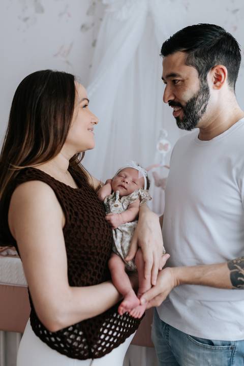 Foto do casal sorrindo um para o outro enquanto seguram a bebê.'