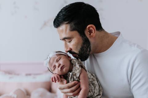 Foto do pai beijando a testa da bebê no quarto.'