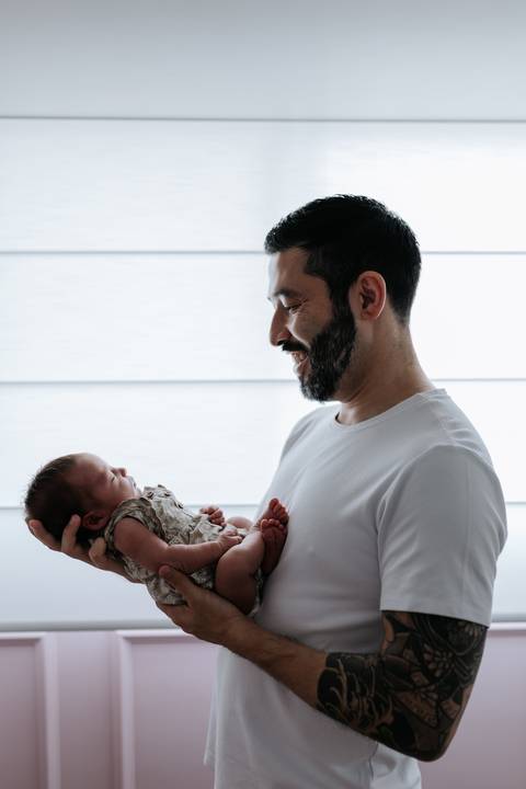 Foto de perfil do pai admirando a filha recém-nascida nos braços.'