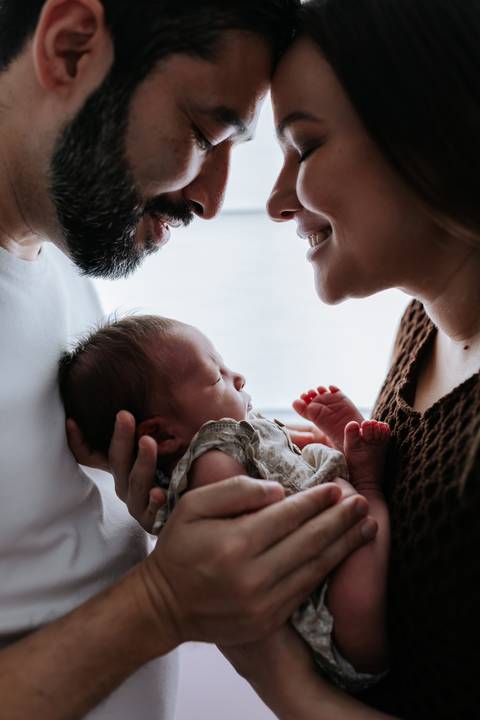 Foto aproximada do casal com o rosto próximo ao da bebê.'