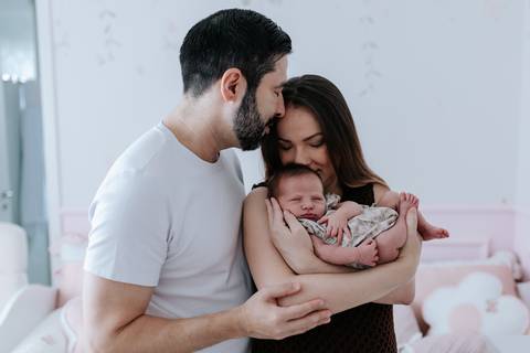 Foto do casal abraçado com a Olívia no colo no quartinho.'