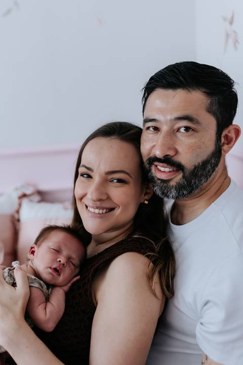 Foto oficial da família sorrindo para a câmera com a bebê.'
