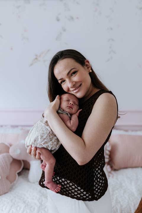 Foto da mãe sorridente com a bebê Olívia no colo.'