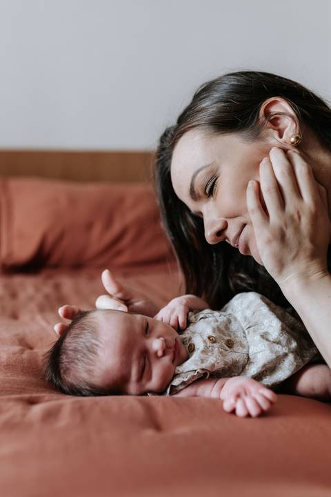 Foto da mãe deitada observando a Olívia com a mão no rosto.'