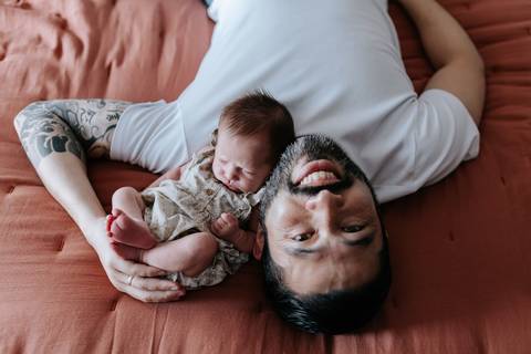 Foto do pai deitado com a bebê Olívia em seu peito sorrindo.'