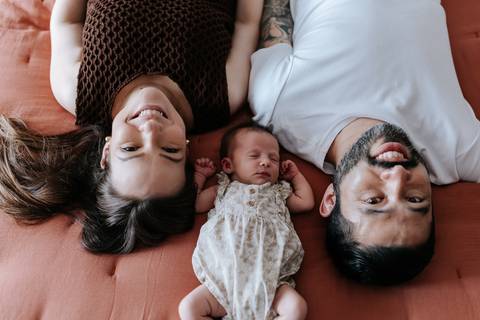 Foto da família deitada na cama olhando para cima em momento lúdico.'