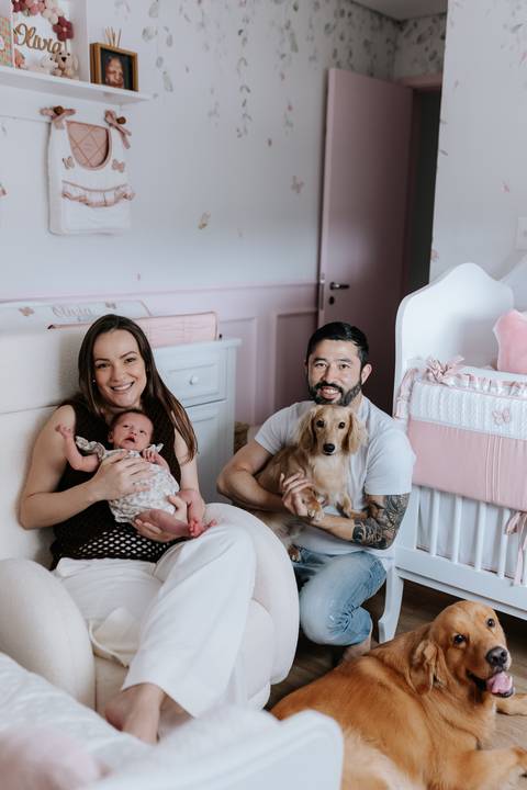 Foto da família sentada no quartinho com a bebê e o pet.'
