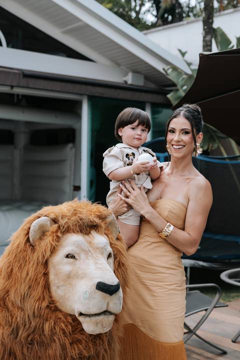 Foto da mãe sorridente segurando o filho próximo à decoração de leão.'