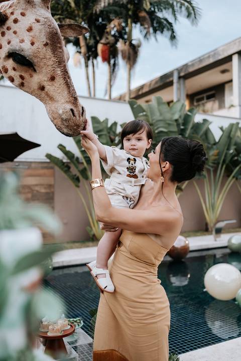 Foto da mãe segurando o aniversariante próximo à escultura da girafa.'