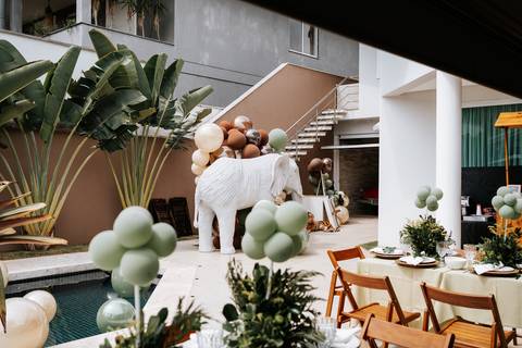 Foto panorâmica da decoração com balões verdes, elefante gigante e mesas postas.'