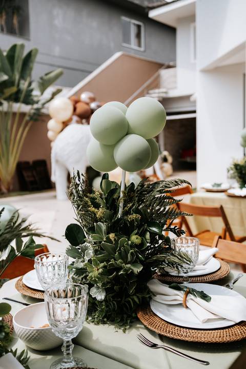 Foto em detalhe de arranjo de mesa com folhagens e balão verde.'