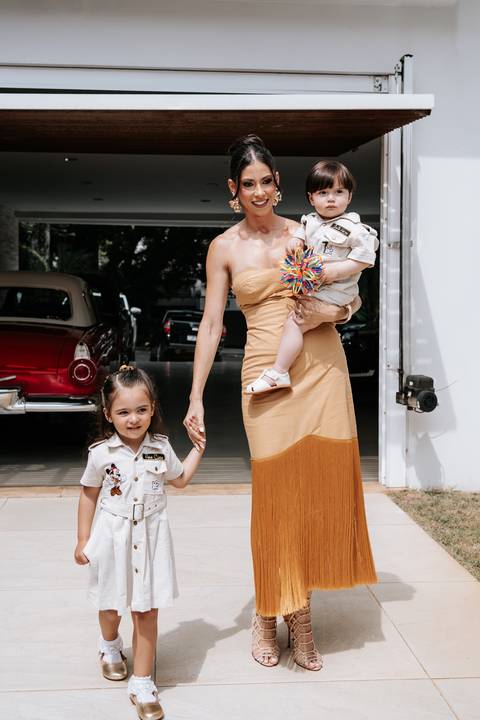 Foto da mãe caminhando com os dois filhos na entrada da festa.'