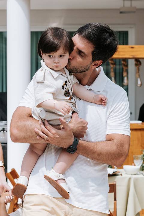 Foto aproximada do pai abraçando o filho pequeno na festa.'