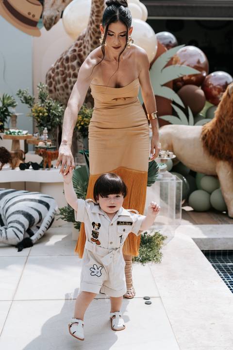 Foto da mãe segurando a mão do pequeno explorador na entrada da festa.'