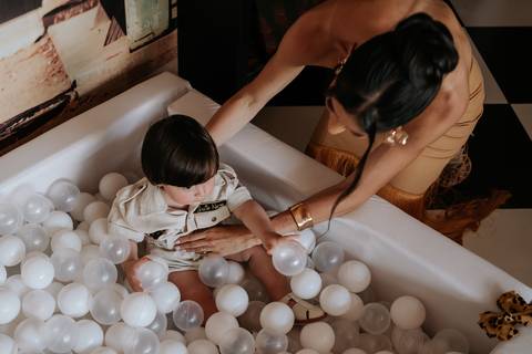 Foto do aniversariante brincando na piscina de bolinhas com auxílio da mãe.'