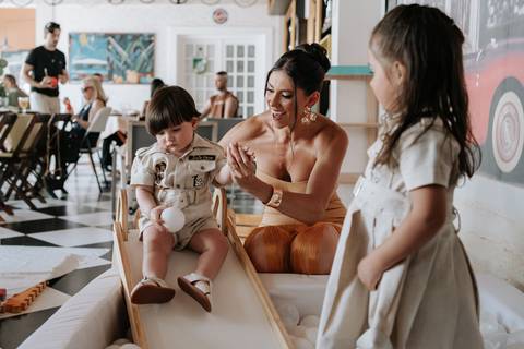 Foto da mãe e filhos brincando no escorregador de madeira da festa.'