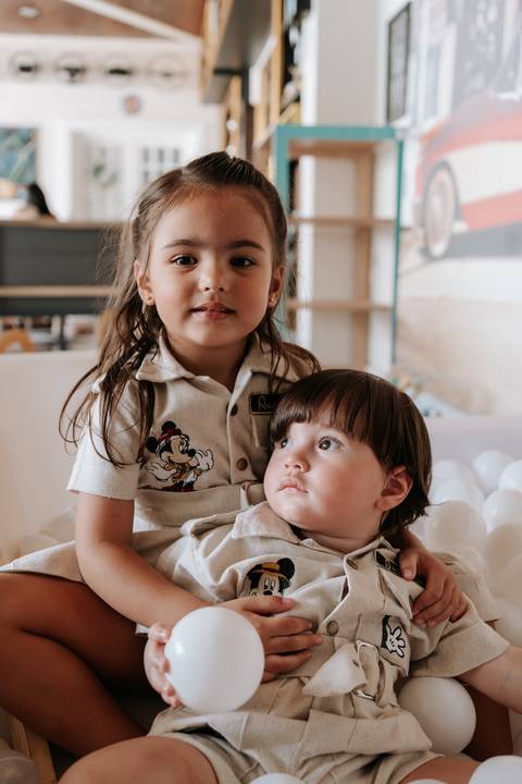 Foto do aniversariante no colo da irmã, ambos com roupas temáticas.'
