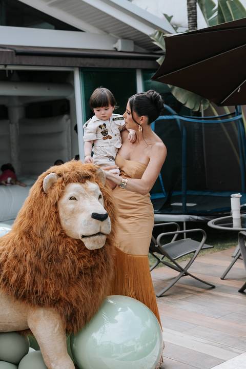 Foto da mãe com o filho no colo posando ao lado da escultura de leão.'