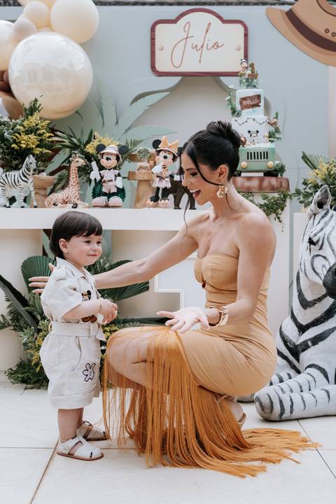 Foto da mãe agachada interagindo com o aniversariante na decoração.'