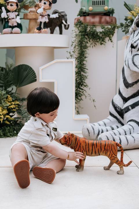 Foto do pequeno explorador brincando com um tigre de pelúcia gigante.'