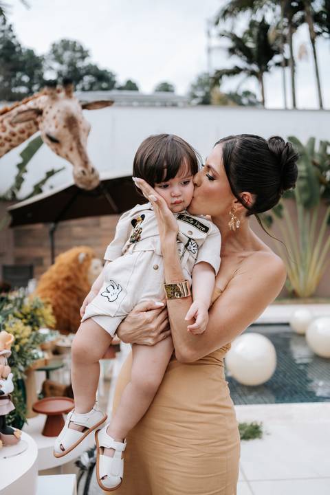 Foto da mãe dando um beijo carinhoso no rosto do aniversariante.'