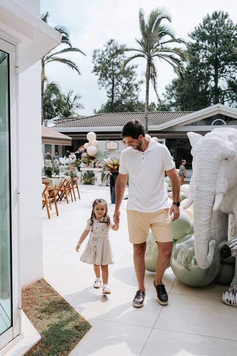 Foto do pai caminhando com a filha pela área externa da comemoração.'