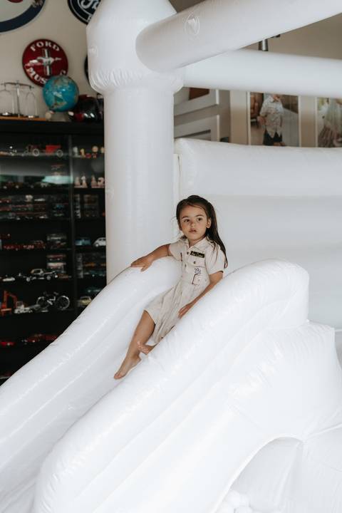 Foto da irmã do aniversariante brincando em escorregador inflável branco.'
