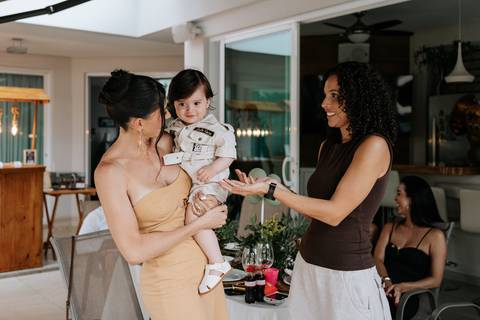 Foto da mãe conversando com convidada enquanto segura o aniversariante.'
