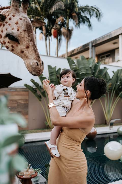 Foto da mãe segurando o aniversariante próximo à escultura da girafa.'