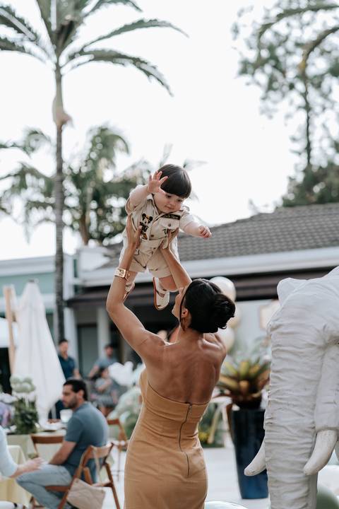 Foto da mãe erguendo o aniversariante para o alto em momento de festa.'