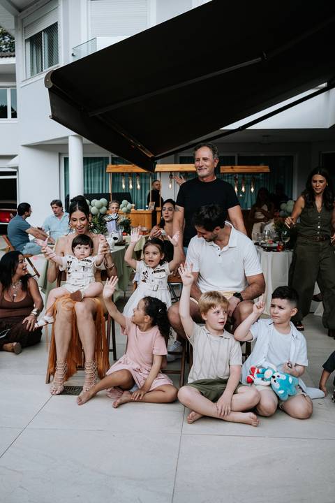 Foto da família e crianças reunidas no chão para as brincadeiras.'