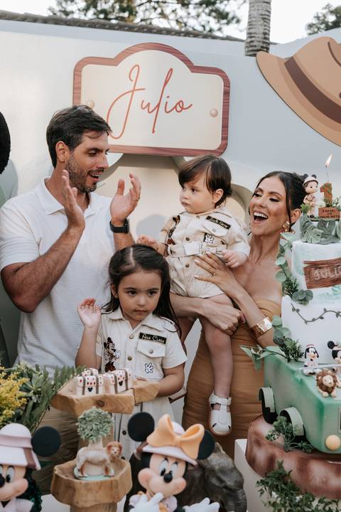 Foto oficial do pai, mãe e filhos batendo palmas em volta do bolo.'