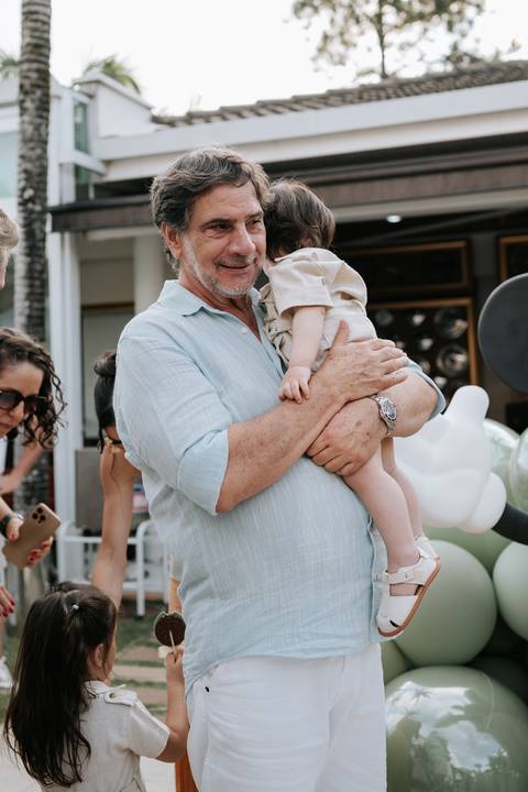 Foto do avô segurando o aniversariante no colo com ternura.'