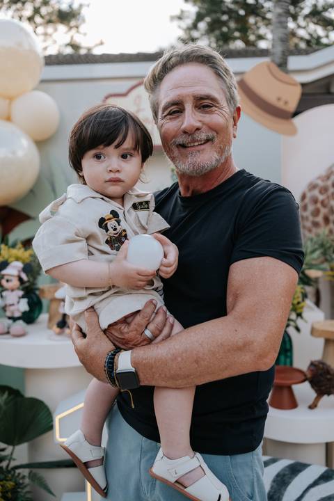 Foto do aniversariante no colo de um familiar segurando uma bolinha.'