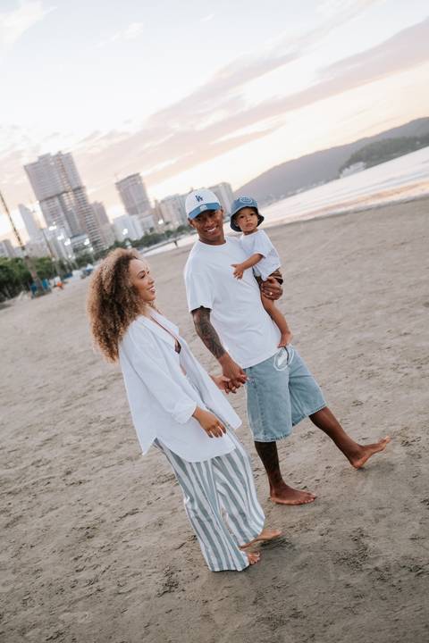 Foto da família caminhando descalça na areia da praia ao entardecer.'