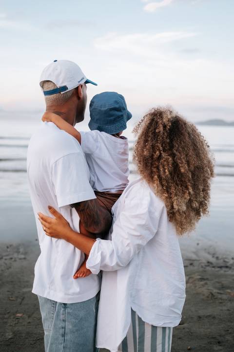 Foto em detalhe das mãos da família unidas na areia da praia.'